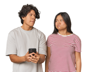 Young interracial couple using smartphone confused, feels doubtful and unsure.