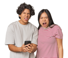 Young interracial couple using smartphone screaming very angry and aggressive.