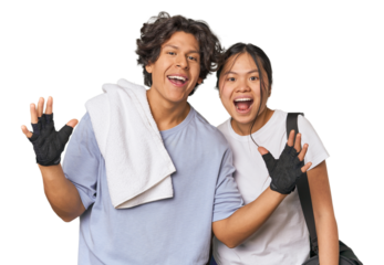 Young interracial athletic couple in studio receiving a pleasant surprise, excited and raising hands.