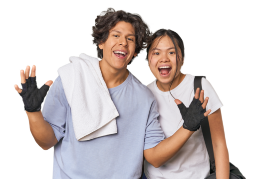 Young interracial athletic couple in studio receiving a pleasant surprise, excited and raising hands.