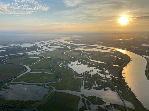 Bird's eye view, aerial photography, at sunset of the Biesbosch national park area in the Netherlands with the sun direct towards the camera looking towards the Dutch coast line showing rivers, lakes 