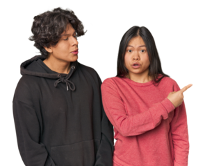 Young interracial couple in studio pointing to the side