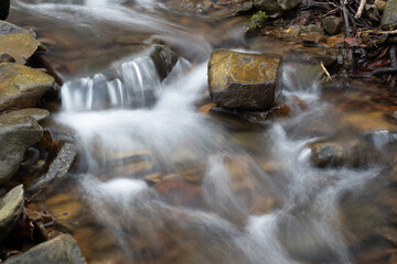 Fototapeta premium Small cascade on mountain stream, wet stone in creek