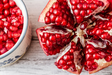 Pomegranate fruit cut open to reveal its juicy red seeds, and a bowl filled with the seeds on a...