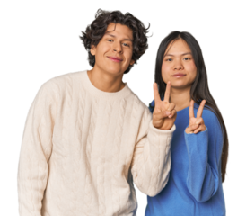 Young interracial couple in studio joyful and carefree showing a peace symbol with fingers.