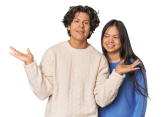 Young interracial couple in studio makes scale with arms, feels happy and confident.