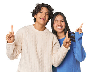 Young interracial couple in studio indicates with both fore fingers up showing a blank space.