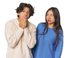 Young interracial couple in studio shocked, covering mouth with hands, anxious to discover something new.