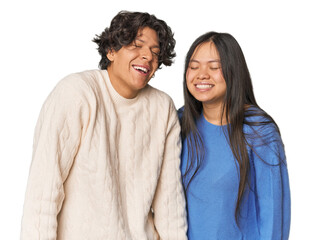 Young interracial couple in studio laughs and closes eyes, feels relaxed and happy.