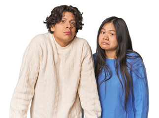 Young interracial couple in studio shrugs shoulders and open eyes confused.