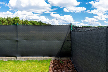 Anthracite-colored masking net placed on a mesh fence, visible pine bark under the fence.
