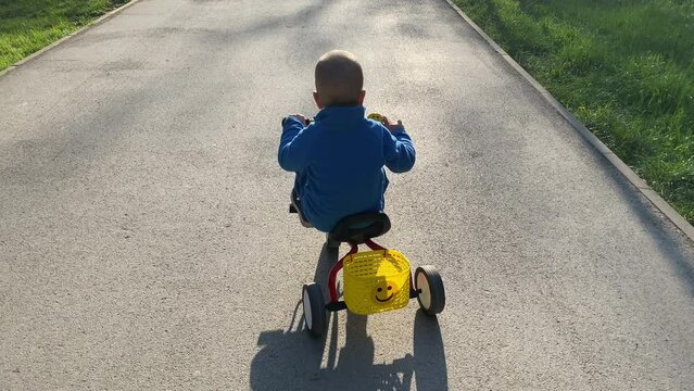 little boy riding tricycle on footpath in summer