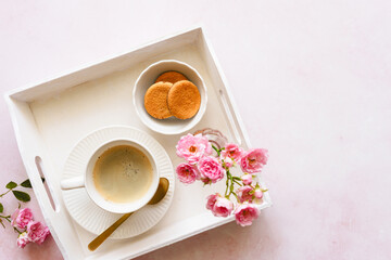 Eine Tasse Kaffee, Kekse auf einem Teller und rosa Blumen auf einem weißen Serviertablett. Pause, Draufsicht.