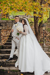 A bride and groom are posing for a picture in front of a tree. The bride is wearing a long white dress and the groom is wearing a suit. Scene is happy and romantic