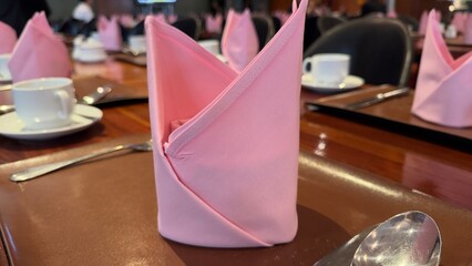 A pink hotel napkin is placed on the dining wooden table.