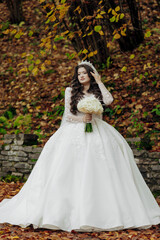 Fototapeta premium A woman in a white dress is holding a bouquet of flowers. She is standing in a forest with leaves on the ground