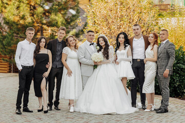 A group of people are posing for a picture, including a bride and groom. The bride is wearing a white dress and the groom is wearing a suit. The group is standing in front of a building