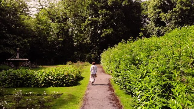 Woman walks through English garden wide aerial drone z