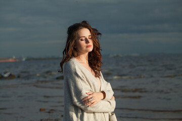 Perfect young lady brunette model on sea beach. Beauty woman with makeup and long dark wavy hairstyle outdoors. Tranquility emotion mood, travel, season and holiday concept