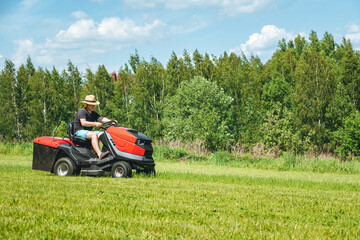 Obraz premium Man on lawn tractor mowing lawn on backyard. The red rider. The lawnmower tractor. High quality 4k footage