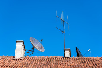 Old Style TV Antennas And Satellite Dish Mounted On Top Of Building Red Tiles Roof