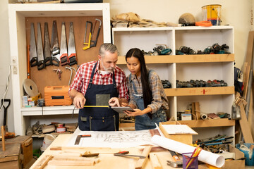 White senior man carpenter doing his work with Asian co worker woman, craft work at furniture factory and copy spcae.