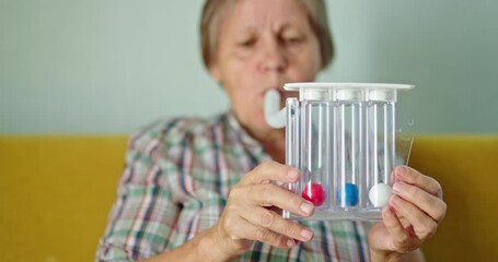An elderly woman blows into a special device - spirometer to train her lungs and test lung capacity
