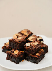 A stack of homemade fudge brownies with almond slices topping on a white plate. Selective focus.