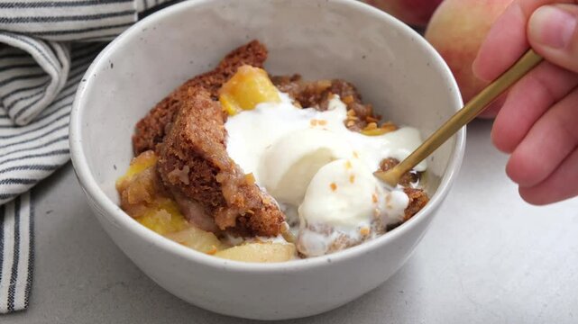 Portion of peach cobbler with scoop of ice cream in bowl.