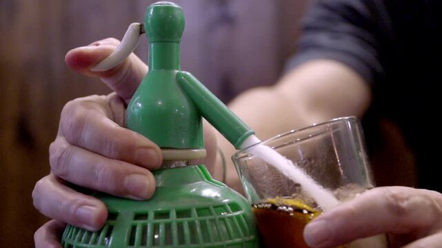 This video captures a person using a vintage green soda siphon to pour a fizzy drink into a glass. The close-up shot highlights the manual process and the carbonation of the beverage.

