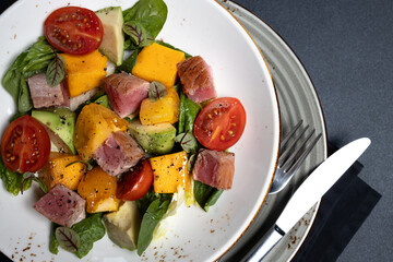Close-up of fresh salad on white plate with black napkin and silverware