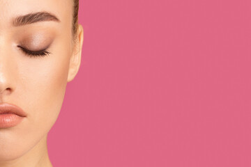Obraz premium Woman half-face with her eyes closed. The woman face is only partially visible, showing her closed eyes, brow, nose, and lips. The background is a solid, bright pink color, copy space