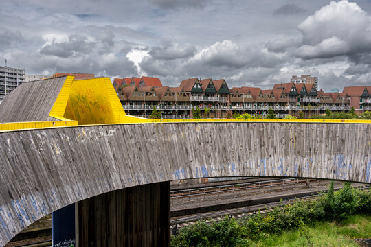 A scenic image showing Luchtsingel a striking wooden bridge with bright yellow accents, overlooking rustic houses with triangular roofs, under a cloudy sky, providing a fine balance of urban and natu