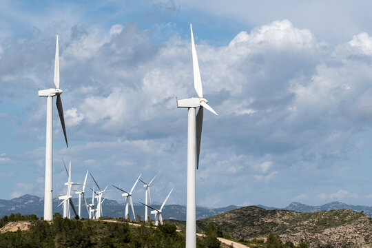 Photograph showing several wind turbines on a hilly landscape under a bright blue sky, emphasizing the importance of green energy and the beauty of renewable resources.