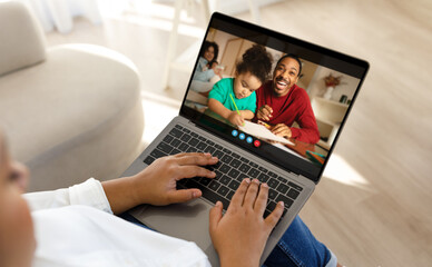 Naklejka premium Black mother is sitting on a couch at home, using a laptop to video chat with their family. The laptop screen shows a father and his daughter, who are both smiling and engaging in a conversation