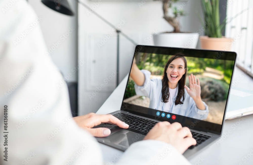 Poster a woman is sitting at a desk in an office setting and video chatting with a person on her laptop. th