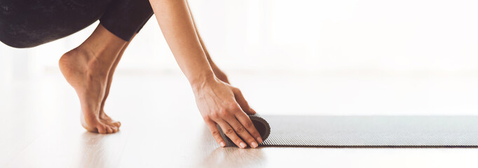 Cropped of woman is caught mid-motion while unrolling a black yoga mat on a clean, white floor, preparing for an exercise session, panorama with copy space
