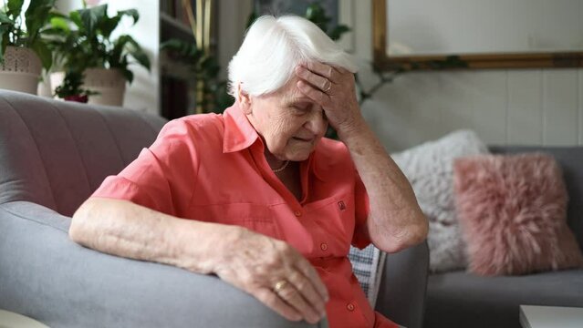Elderly woman sitting in armchair suffering from headache 
