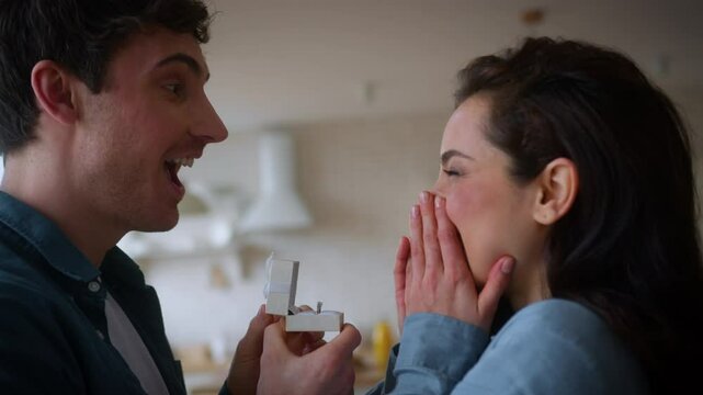 Lovely happy smiling couple love affection romantic feelings Caucasian man guy male present ring ask marry me propose bride woman girl female say yes agree at home celebrate engagement wedding hugging