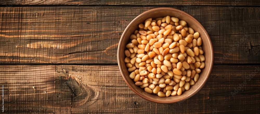 Aufkleber Top view of a bowl with pine nuts on a wooden background, providing space for a text overlay or other elements in the image. copy space available