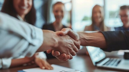 A handshake between a businessman and businesswoman in a modern office, sealing a successful deal, with colleagues smiling in the background and laptops and documents on the table, showcasing