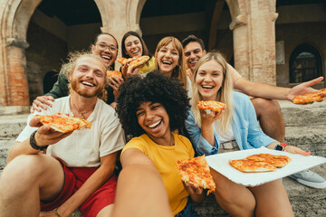 Multicultural smiling friends eating pizza sitting outside - Cheerful young people taking selfie photo with smartphone outdoor - Happy life style concept with guys and girls hanging out on a sunny day