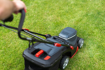 Fototapeta premium Machine for cutting lawns. Lawn mover on green grass in modern garden. Man using modern garden tools