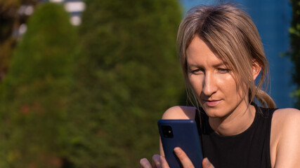 Close-up of a focused young blonde woman with a ponytail reading and typing a message on a mobile...