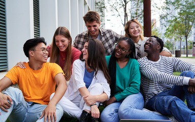 Multiracial group of student friends gathering outside university campus after classes, talking,...