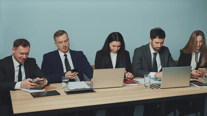Business professionals sitting at conference table during work break, all focused on their smartphones. Impact of mobile addiction and distraction in workplace. Concept mobile addiction