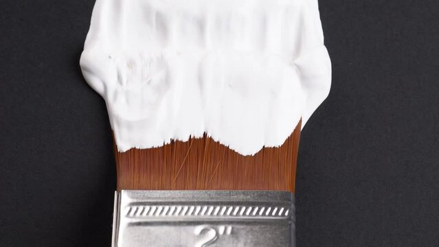 White painting brush strokes. Painting white vertical strokes on black paper, macro shot. Close up of artists hand holding paint brush and drawing gouache or oil painting.