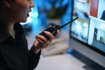 Security worker talking by radio with colleague while sitting in front of monitor and watching for...