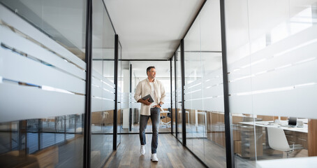 Mature professional executive business man walking, holding, using laptop pc or tablet at modern company office workplace space. Full body portrait of confident smiling senior businessman, copy space