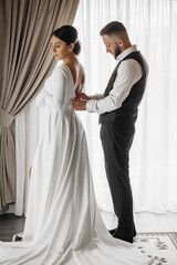 Fototapeta premium A bride and groom are standing in front of a curtain, with the bride wearing a long white dress